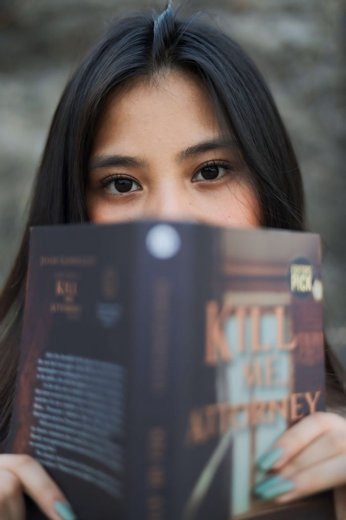 Close-up of a woman with black hair intensely reading a novel outdoors.